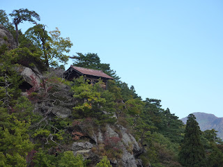 Photo over the side of the mountain with a temple building on the edge of a cliff