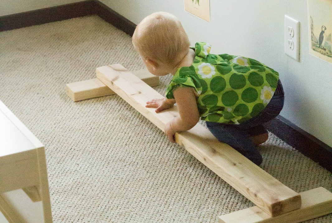 Young toddler plays with a DIY wooden balance beam in her Montessori home.