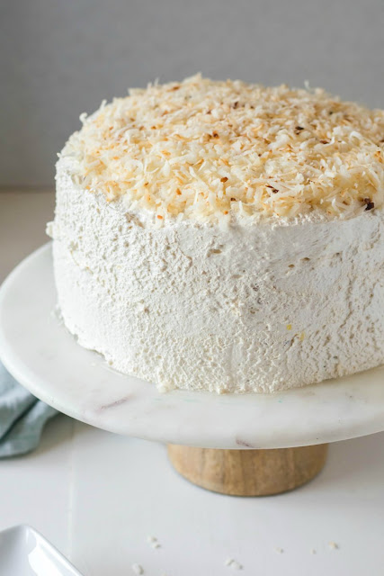 This cake is amazing! It is LOADED with pineapple and then coated in a big white cloud of frosting. Add a little coconut to drive the taste of the tropics home! haleakala cake with toasted coconut on top on a marble and wood cake stand