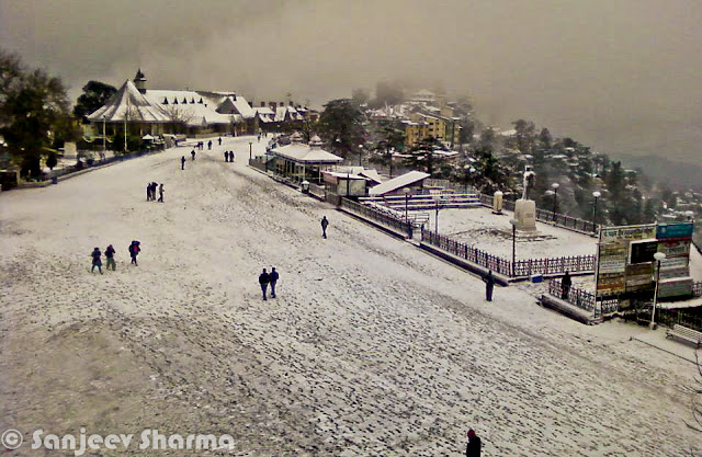 Shimla has been getting snowfall since 5th January 2012 and Sajeev has been capturing each moment of post-snowfall moments at various places around Shimla - Mall Road, Ridge ground, Scandal point, Lakkar Bazar etc. This year Shimla is getting heavy snowfall and some of the evidences can be seen in this Photo Journey from last week... Sanjeev Sharma with unknown Cameraman, Zee news, Shimla :)Sanjeev himself on Ridge Ground, while it's snowing on Ridge Ground, Shimla, Himachal Pradesh, India. You can see Christ Church on one corner of the Ridge and Shimla Library adjacent to it. Somehow Shimla is known by these two buildings. Yesterday only I saw fridge magnet at Connaught Place, Delhi with these two buildings carved on a marble piece to make a souvenir of Shimla, Himachal Pradesh. There were lot of other stuff form various cities of India like Jaipur, Varanasi, Maisoore etc.Here is a photograph with footmarks of people who were enjoying fresh snowfall on Ridge Ground and left for their homes.Although there are still few folks roaming around. Whole sky is covered with dense mist or clouds. The leading path is actually touching Mall Road, which is one of the main places people love to roam around in Shimla. buildings on left side are Goofa Restaurant and Bar by HPTDC and Gaitey Theatre, which was renovated last year only.Here is a closer look to Goofa Restaurant and Bar. One of the decent place to have dinner on Ridge Ground, although our experience of Goofa bar was not so good, when we were in University. But this is considered one of the decent places..Business in Snow... The famous Krishna bakers is closed but 100 Pipers and other brands of whiskey are available. And probably Rum would be more demand in such a lovely snow. Just notice the height of snow on the road... All these shops are located on lower part of the Mall Road...Another view of ridge Ground from an elevated boundary which leads towards Jakhu Temple, Shimla.Snow was on and off during last 10 days and yesterday there was heavy snowfall, which made people comment negatively about it. Till yesterday everyone from Shimla was putting happy and interesting statuses about Snowfall on facebook. But suddenly things changed yesterday when this snow started impacting lives of people in Shimla. For tourists, heavy snowfall can be good but for loacl folks it creates lot of problems at times. Water and Electricity supply is one of the main challenge during heavy snowfall hours. Notice the forest behind Mr. Sanjeev which are still white and these high deodars look amazing with snow on top of themPath created by Ambulance is being smartly used by these folks. vehicles are not allowed on Ridge Ground and Mall Roads.. Only Ambulance or police vehicles are allowed as and when required. Although many bollywood movies have shown vehicles flying on ridge ground. All that is done after special permissions from Shimla Authorities.Here is a a view of Shimla Ice Skating Club, which is located just below Lakkar Bazar, Shimla. This club is also visible from top of Indira Market on Ridge Ground. During December a national level event is organized, where lot of professionals come to this club for showing their Ice Skating performances. Even without ice these folks from Shimla can be seen on Mall Road and Ridge on  every Saturday :)Evening view of Ridge with spoiled snow... Place like Shimla are enjoyable either during fresh snowfall or without any snow. After 2 or 3 days of snowfall, snow melts or take a shape of huge pieces of ice which are risky to walk and dirty as well. During that time, snow in places are Kufri or Narkanda is more enjoyable. In fact, these days Skiing training is going on at Dhomri, Narkanda...Mr. Sanjeev, covered with multi-layered cloths and posing for a photograph against scandal point. Scandal point is a place from where two roads are diverted - one towards Ridge ground and other continues as Mall Road towards Shimla Town Hall and Gaiety Theatre.Gukli just stood up for this photograph, otherwise he must be busy in making snowman or playing snowballs :) ... Smile on his face is telling about the excitement about fresh snowfall in Shimla.Every year tourists come to Shimla during last week of Decemeber in a hope of Snowfall, but now timings have shifted a bit. For last few years, Shimla is getting snowfall in second week of January or towards end of first week.This year (2012), it was first time that some of the regions in Himachal got snowfall. Places like Hamirpur were also covered with white sheet of snow, although it remained only for few hours and then disappeared. At the same time various places of Kangra District got snowfall - Nagrota, Palampur, Dharmshala and Kangra town itself. Kangra Twon got snowfall after 52 years...Sanjeev is still waiting for his car to be uncovered of Snow Blanket... Try to imagine, how people in Shimla must be commuting to their offices and other places for some work... Conditions get worse in case of continuous snowfall for longer period of time.Many businessmen in Shimla make more money during tis season but at the same time, many folks with small setups loose lot of business due to heavy snow. I am sure that every weekend Shimla is getting lot of tourists from Punjab and Delhi...Sanjeev in perfect pose for this photograph with snow in the background :) (Shimla, Himachal Pradesh, India)Another amazing view of Ridge Ground covered with Snow and few folks walking on it... I still remember the day when I saw snowfall first time and we came to Mall Road for playing with snowballs... Everyone from our class was on Mall Road and whole day was full of fun and enjoyment....Sanjeev looks pretty happy and hopeful about this snowfall... Probably he is done with his walk on Mall Road and moving towards Press Club at Indira Market on Ridge ground of Shimla TownHere is last and wonderful photograph of this amazing Photo Journey by Sanjeev Sharma. Hope that snowfall comes with happiness and keep whole environment cheerful without any damage to anyone. And if you are amongst ones who have never seen snowfall, this is right time to plan your trip to Shimla and enjoy it.Thanks a Lot Sanjeev Sharma for such a Lovely Photo Journey with full of life photographs from last one week.