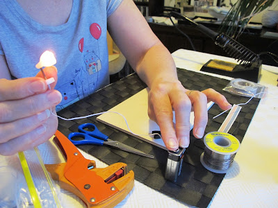 Woman holding a modern dolls' house miniature lamp, lit from wires connected to a 9-volt battery.