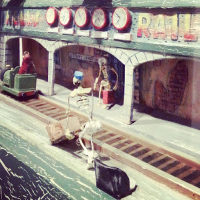 Model skeleton pushing a trolley of baggage at a miniature ghost train.