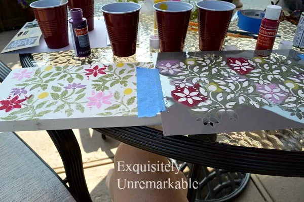 Stenciling A Board on a picnic table with red solo cups and paint supplies