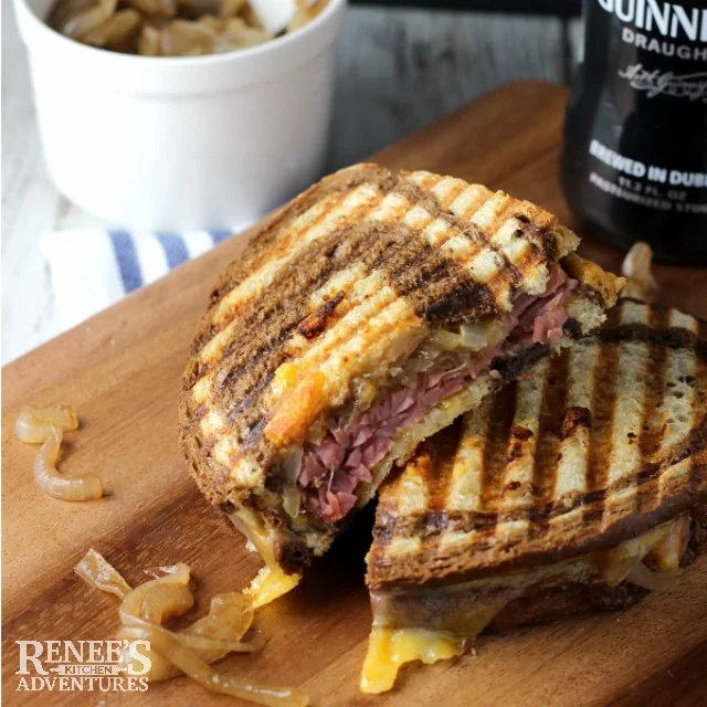 Corned Beef Panini with Caramelized Guinness Onions cut in half and placed one half on top of the other on board