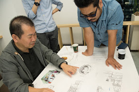 This photo, which accompanied an interview with Yu Suzuki & Katsuhiro Harada, shows Yu with various Shenmue design documents as he points at what appears to be a sketch of a Chinese tulou.