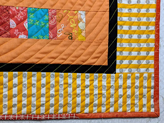 The border and the various orange prints used to bind the quilt are shown.