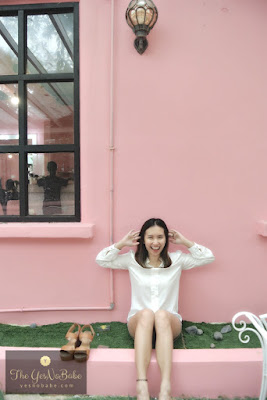 She sits on the grasswith her shoes off lying on the pink wall behind her at Once Upon A Time Cafe Johor Bahru
