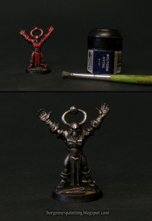 Photo showing a miniature with more concentrated, red overlay representing stippling - with a flat, round brush - with a said brush and a pot of Boltgun Metal paint visible on the right.