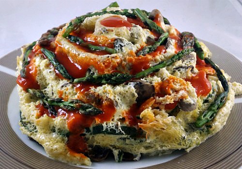 Pastel colorido de verduras adornado con puntas de espárragos y salsa de tomate
