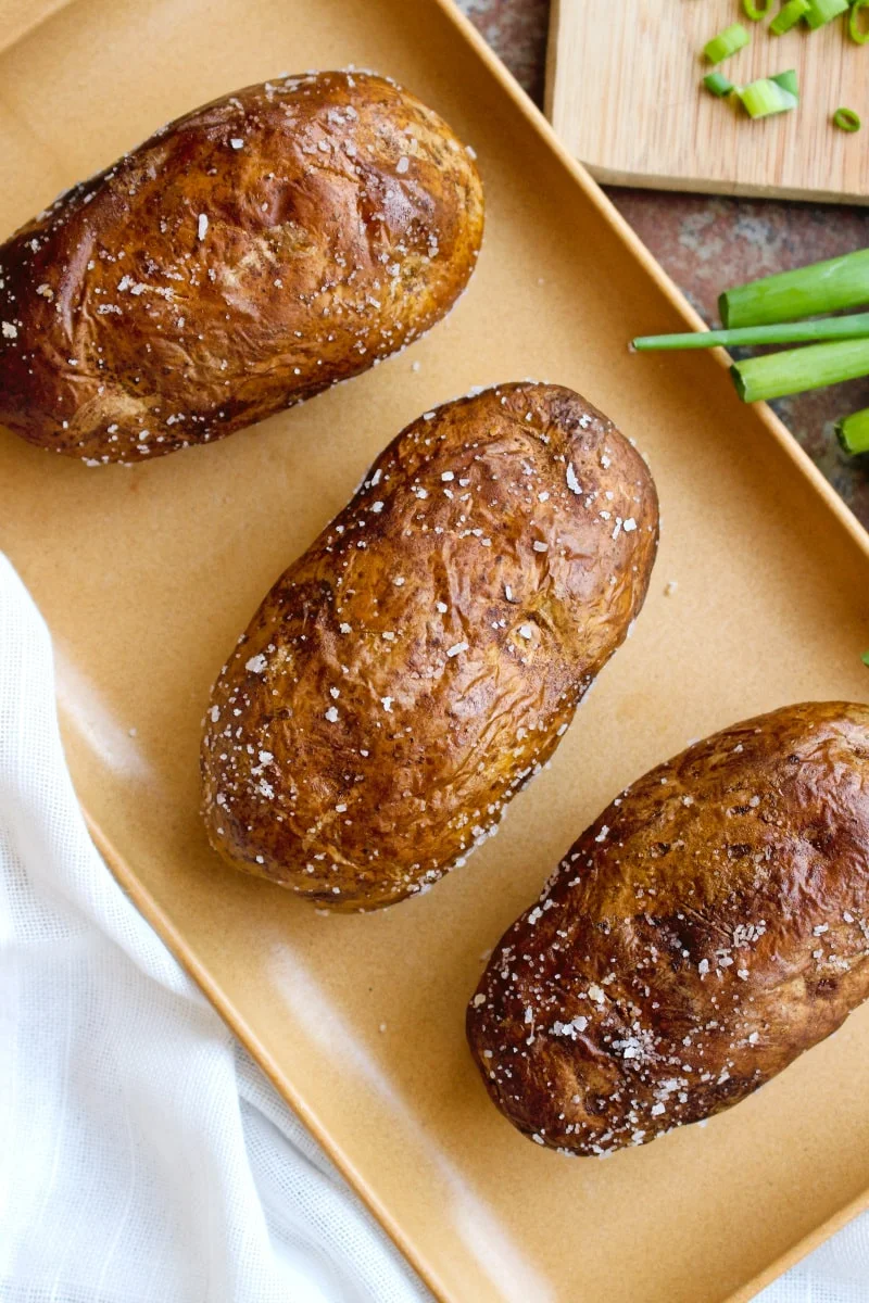 These baked potatoes cooked in the air fryer have a perfectly cooked fluffy inside and an irresistible crispy salty skin. You can eat them as a side dish or enjoy them as a light main dish! #airfryer #bakedpotato #sidedish