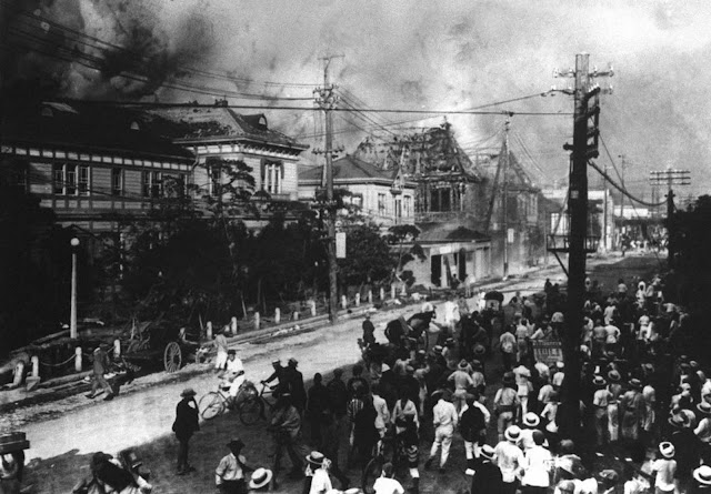 As pessoas se refugiam em uma rua Nihonbashi, no Japão, em 1923. Os prédios do outro lado da rua estão queimando e subindo fumaça e chamas de um terremoto que atingiu.