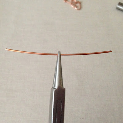 Piece of wire held in middle by round nose jewelry pliers