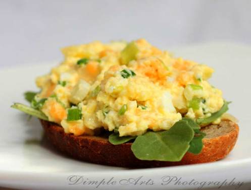 This open faced egg salad sandwich served on a bed of spinach and fresh bread is tasty.