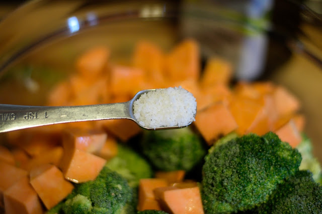 Salt being added to the bowl of prepped broccoli and sweet potatoes. 