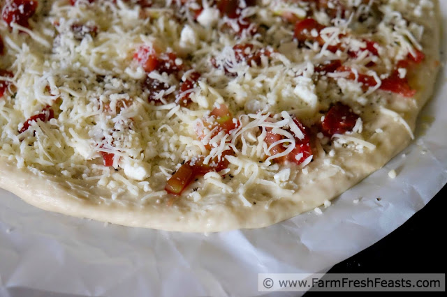 a photo of pizza dough topped with cheese and heirloom tomatoes, ready to be grilled