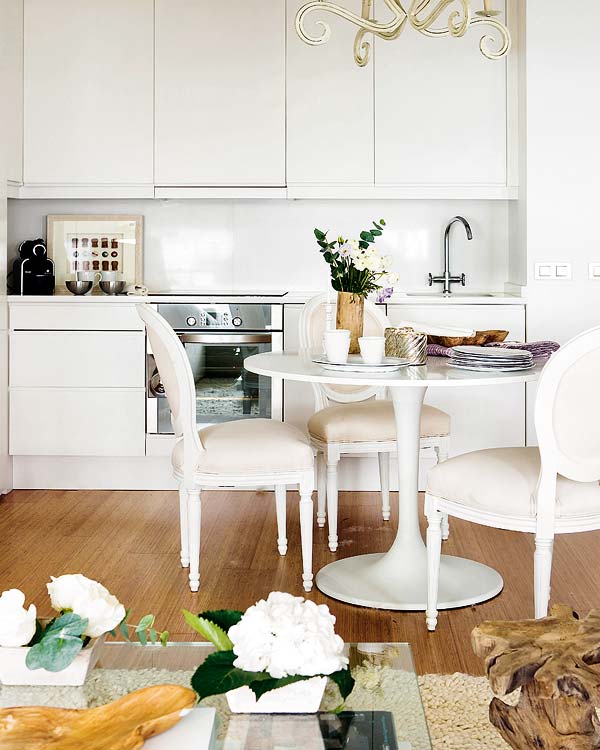 Kitchen in a tiny apartment with wood floor, white Louis XIV chairs, stainless appliances, white cabinets and white countertops