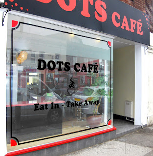 Black vinyl boarder around two display windows with red quartered circles in the corners. Bold black text with 'Dots Café' & a steaming coffee logo in the main window.