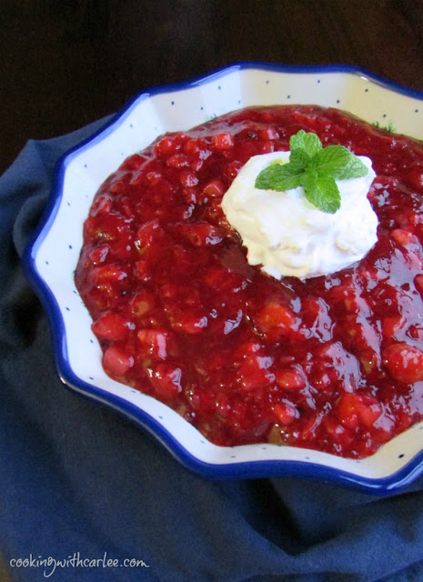 This fun cherry pineapple "salad" is sure to be a hit with your family. It is a simple make ahead side dish that is festive for a holiday or fun for a BBQ. bowl of cherry pineapple jello topped with whipped cream and fresh mint