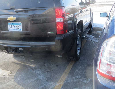Black SUV with FlexFuel logo, exhaust coming out of pipe, parked over the yellow line