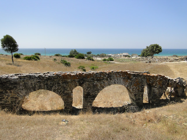 Acueducto de ladrillos romano con vegetación mediterránea en verano y el mar al fondo.