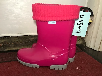 A pair of pink wellies with a roll top liner and labels still on next to a front door