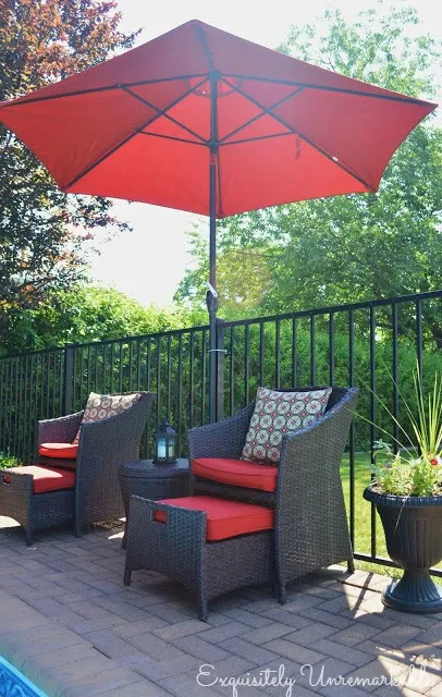 Wicker chairs with red cushions and pillows under a red umbrella