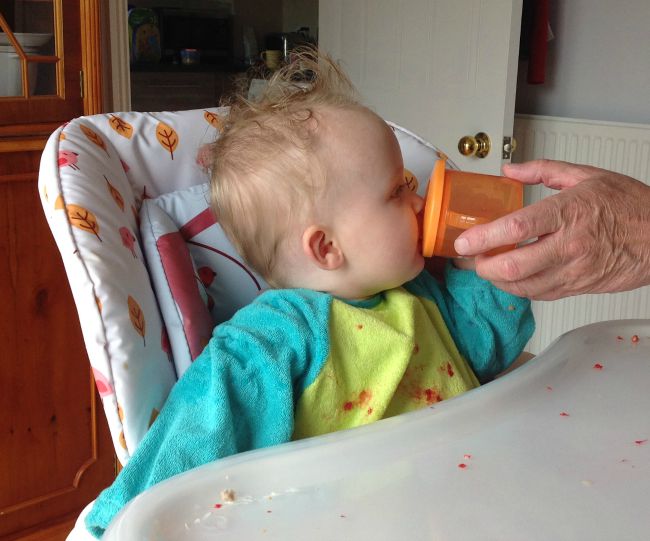 How-to-open-a-Tommee-tippee-sippy-cup-without-breaking-your-nails-image-of-orange-tommee-Tippee-cup-and-baby-in-highchair-drinking-from-orange-cup