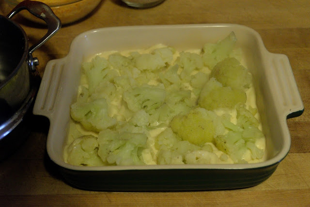 Cooked cauliflower being added to a baking dish. 