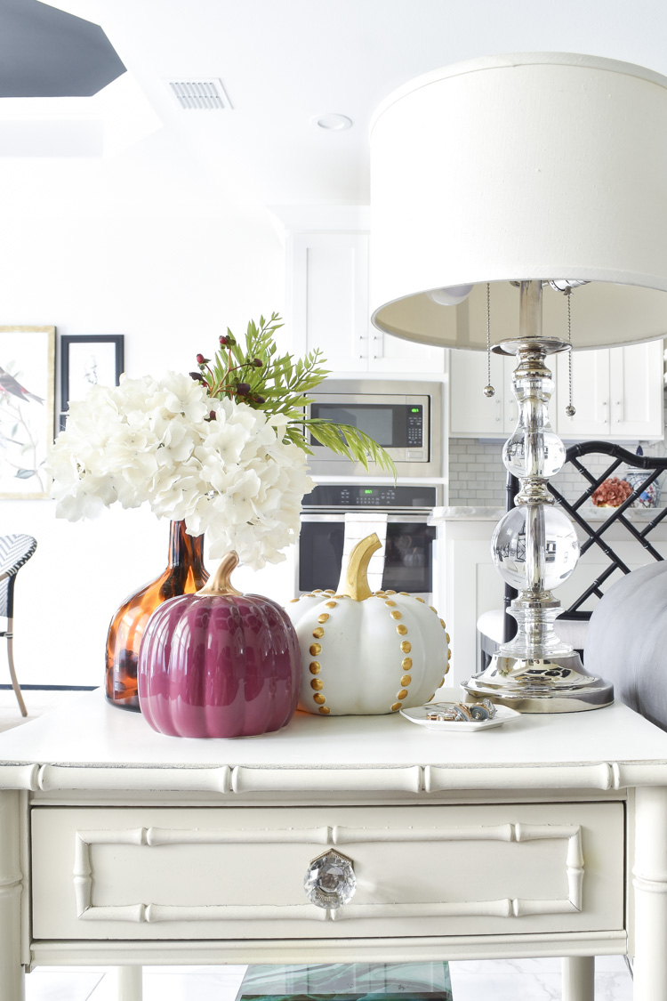 A white bamboo end table with fall decor, hydrangeas and pumpkins in an eclectic living room A white bamboo end table with fall decor, hydrangeas and pumpkins in an eclectic living room