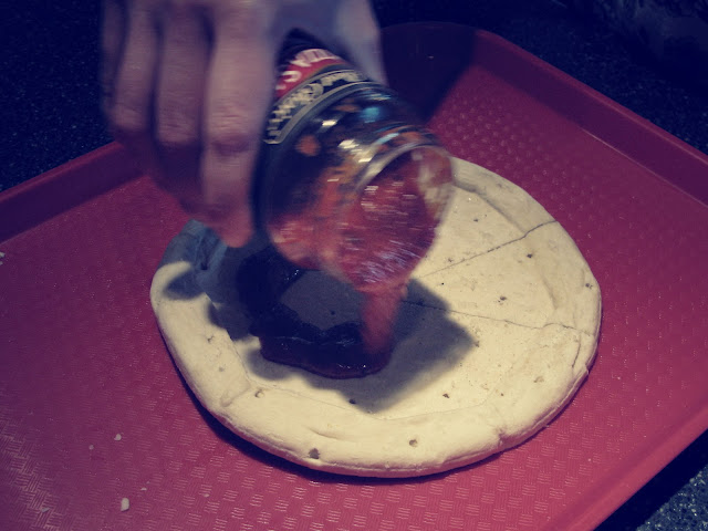 Showing the slice cut out of the pizza crust and putting pizza sauce on the crust.