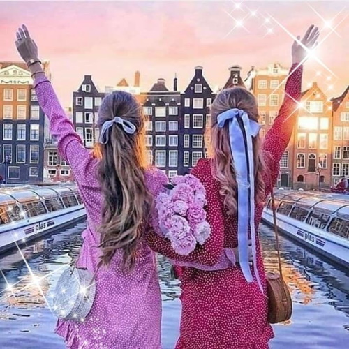 Se você conhece o autor desta imagem, por favor nos informe para que possamos atribuir-lhe os devidos créditos. Obrigado. #PraCegoVer: Duas jovens acenando com flores na mão, Olhando a paisagem ao longe com prédios, como se estivessem se despedindo do lugar ou de alguém.