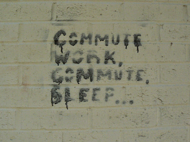 Graffiti on a wall reading Commute Work, Commute Sleep....