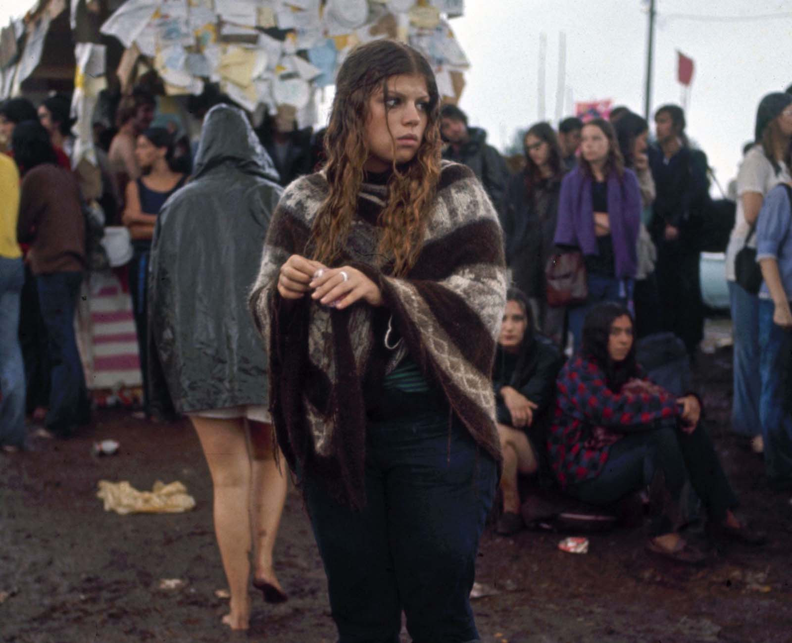 A bedraggled young woman stands in the mud on the grounds of the Woodstock Music & Art Fair.