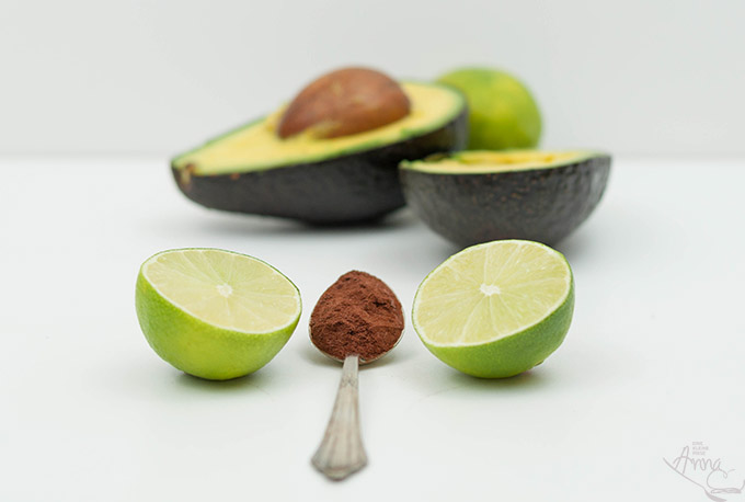 Avocado, Limetten und Kakao Aufgeschnittene Avocado mit Limettenhälften und einem Löffel Kakao