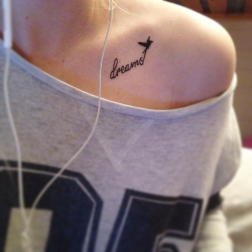 Chica usando una camisa gris y mostrando su tatuaje de una frase en ingles en el hombro