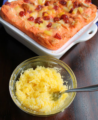 pan of puffy pink bread pudding with bowl of golden coconut topping ready to be spread on top