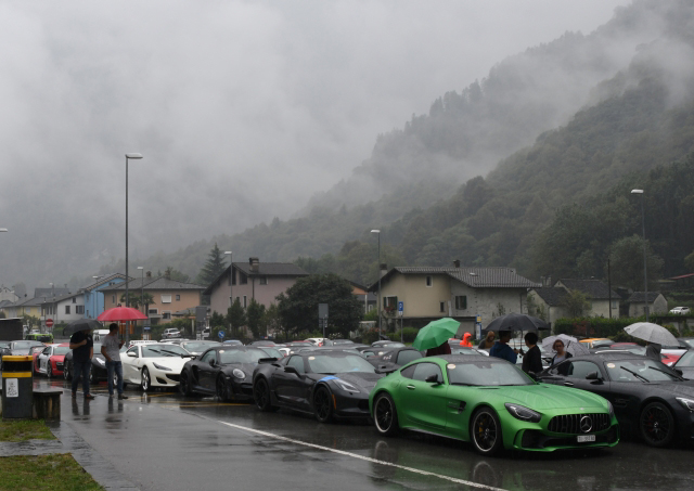 100 Autos auf einem Parkplatz. Leider mit Nebel und Regen. Grüner Mercedes AMG und andere Teilnehmer des Sportcars Day auf dem Parkplatz in Cevio. Tiefe Wolken, Nebel, Regen