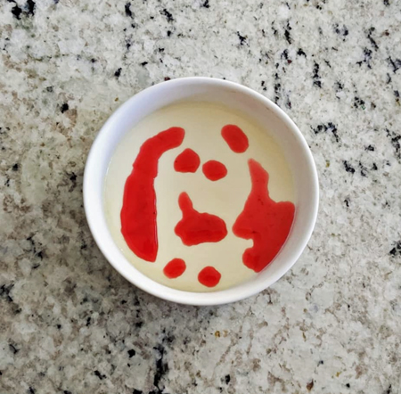 image of a bowl of panna cotta with bright red sauce dripped on top, sitting on my kitchen counter, photographed from above