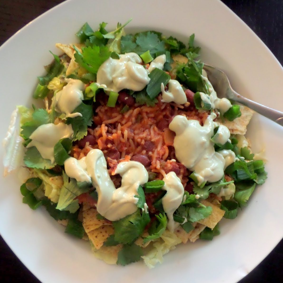 Bean and Rice Taco Salad:  A vegetarian meal of tortilla chips and lettuce, topped with spicy rice and beans, and finished with avocado sour cream and cilantro.