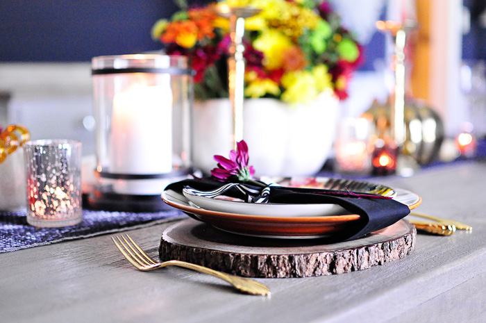 A rustic glam fall floral tablescape featuring a bold floral pumpkin centerpiece, acacia wood chargers, black and white striped dinner plates and leaf salad plates paired with vintage gold flatware. A colorful, metallic glam look perfect for any fall dining table. 