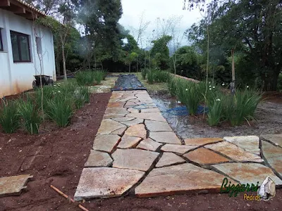 Execução do caminho de pedra no jardim com pedras Goiás com execução do paisagismo com mudas de moréais em residência em Piracaia-SP.