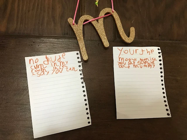 A brown wooden door with a M on it and two pages ripped out of a notepad. The notes say "No bude cum in my room inles I say you can" and "Your the moost menist you are sophie and mummy"
