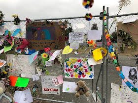 Cards, flowers, and drawings of sympathy and support attached to a fence