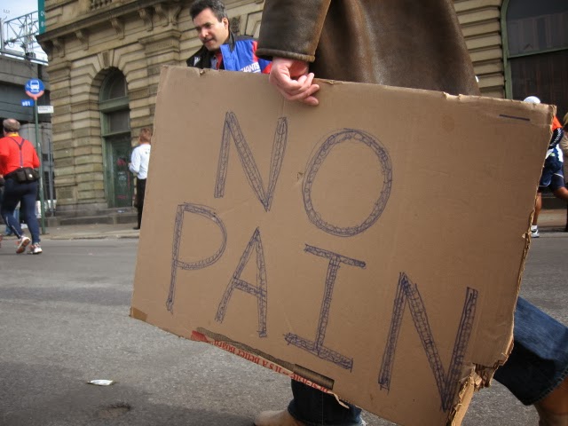 Photograph of man holding a sign reading "No Pain"