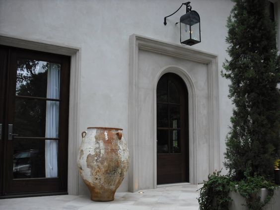 Antique French urn at entrance of grand stucco home with black trim and accents.