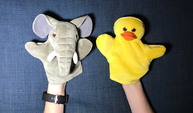 Hand Puppets A small elephant hand puppet and a bright yellow duck puppet on the end of arms on a blue fabric background