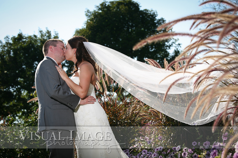 Groom kissing bride with long sunlit veil in Frame Park