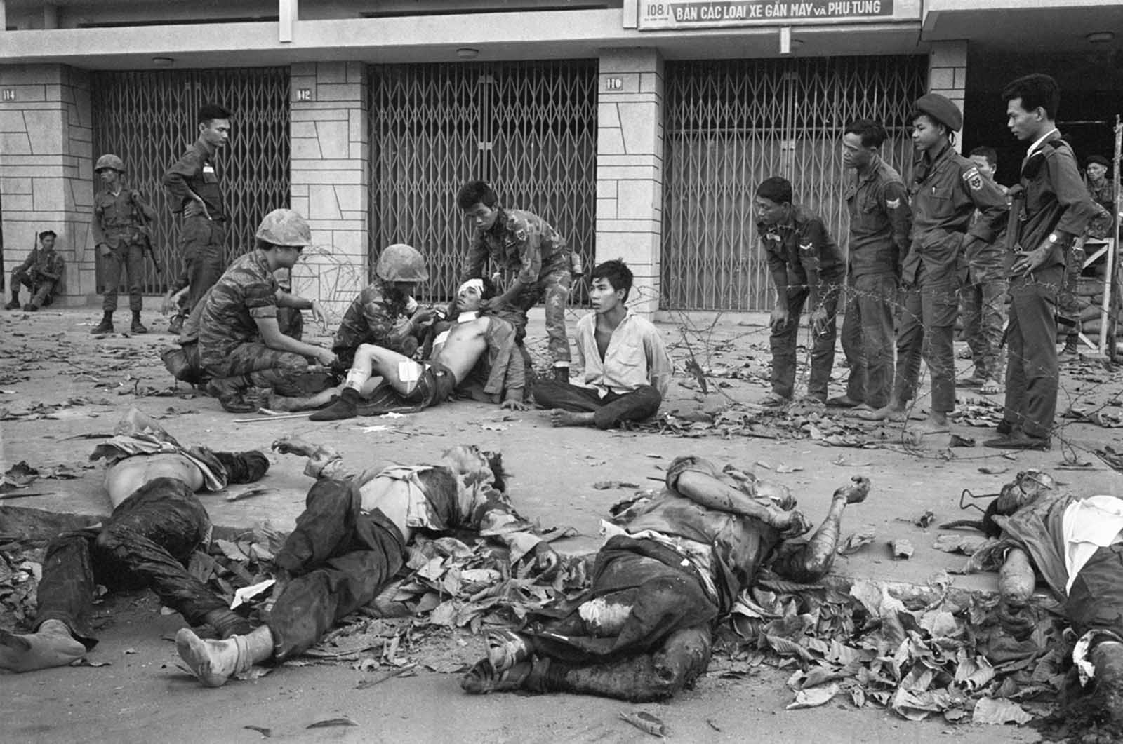 A Viet Cong prisoner sits next to corpses of 11 of his slain fellow guerrillas after a street fight in Saigon-Cholon on February 11, 1968. In the background are Vietnamese Marines that defeated a Viet Cong platoon holed up in the residential area. The prisoner was later taken out for interrogation.
