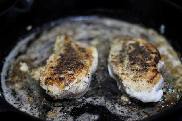 The chicken breasts in the skillet have been flipped and you can see the golden brown crust of garlic and herbs