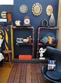 One-twelfth scale miniature lounge area with a set of pipe shelves containing books and ornaments and a black egg chair.